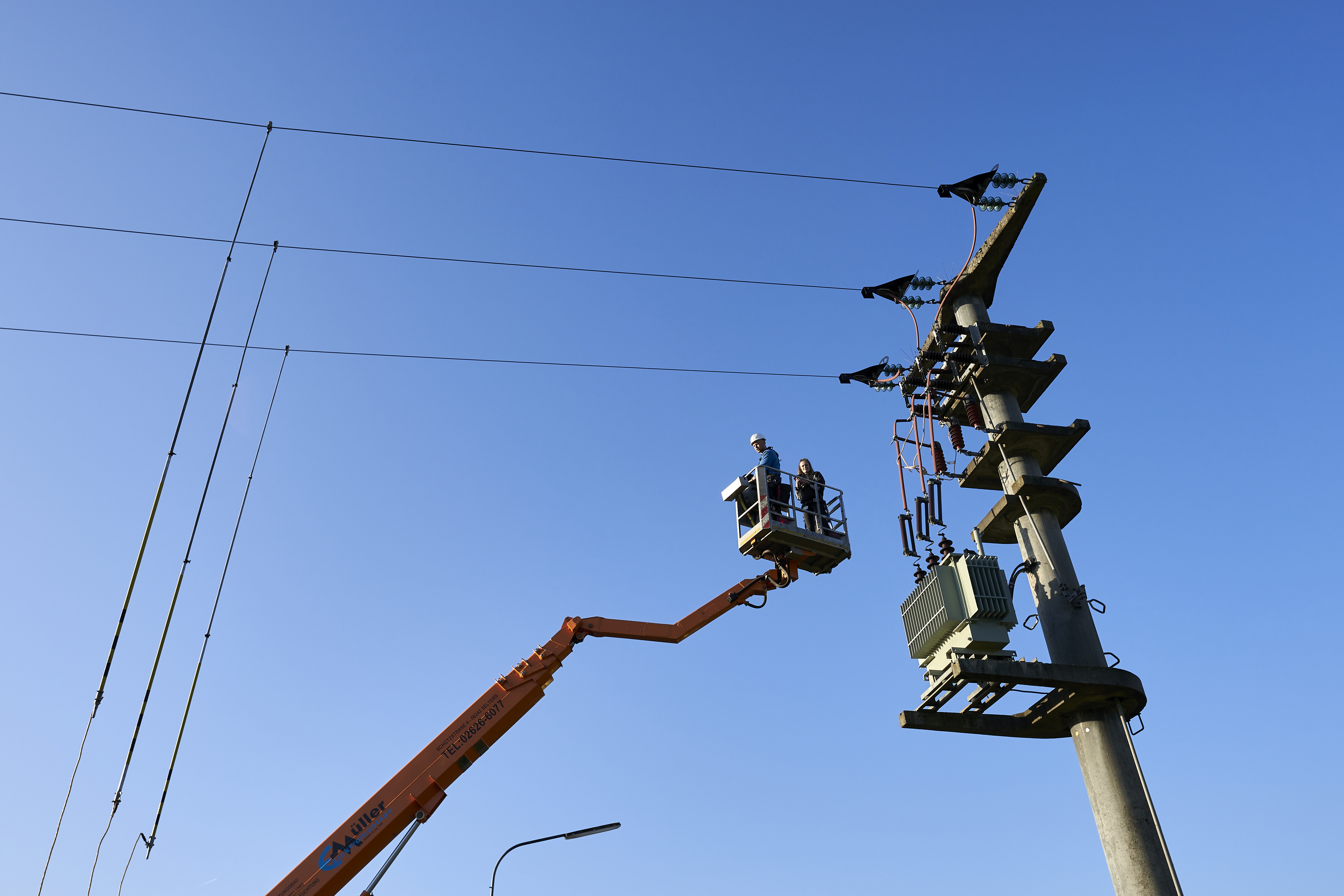 enm-Arbeiter arbeiten auf einer Arbeitsbühne an einem Strommast.