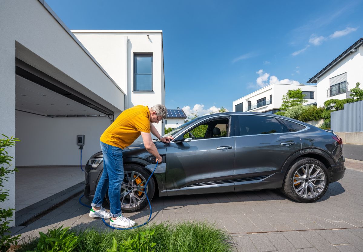 Ein Mann mit gelbem T-Shirt steht vor einem E-Auto und hält einen E-Ladeschlauch