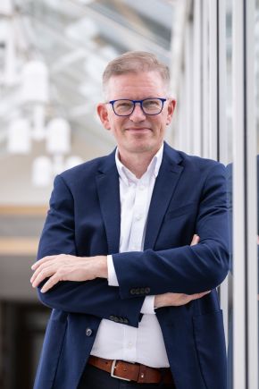 EVM-2025-142_angepasst Ein Mann mit Brille ist professionell gekleidet und lächelt freundlich.