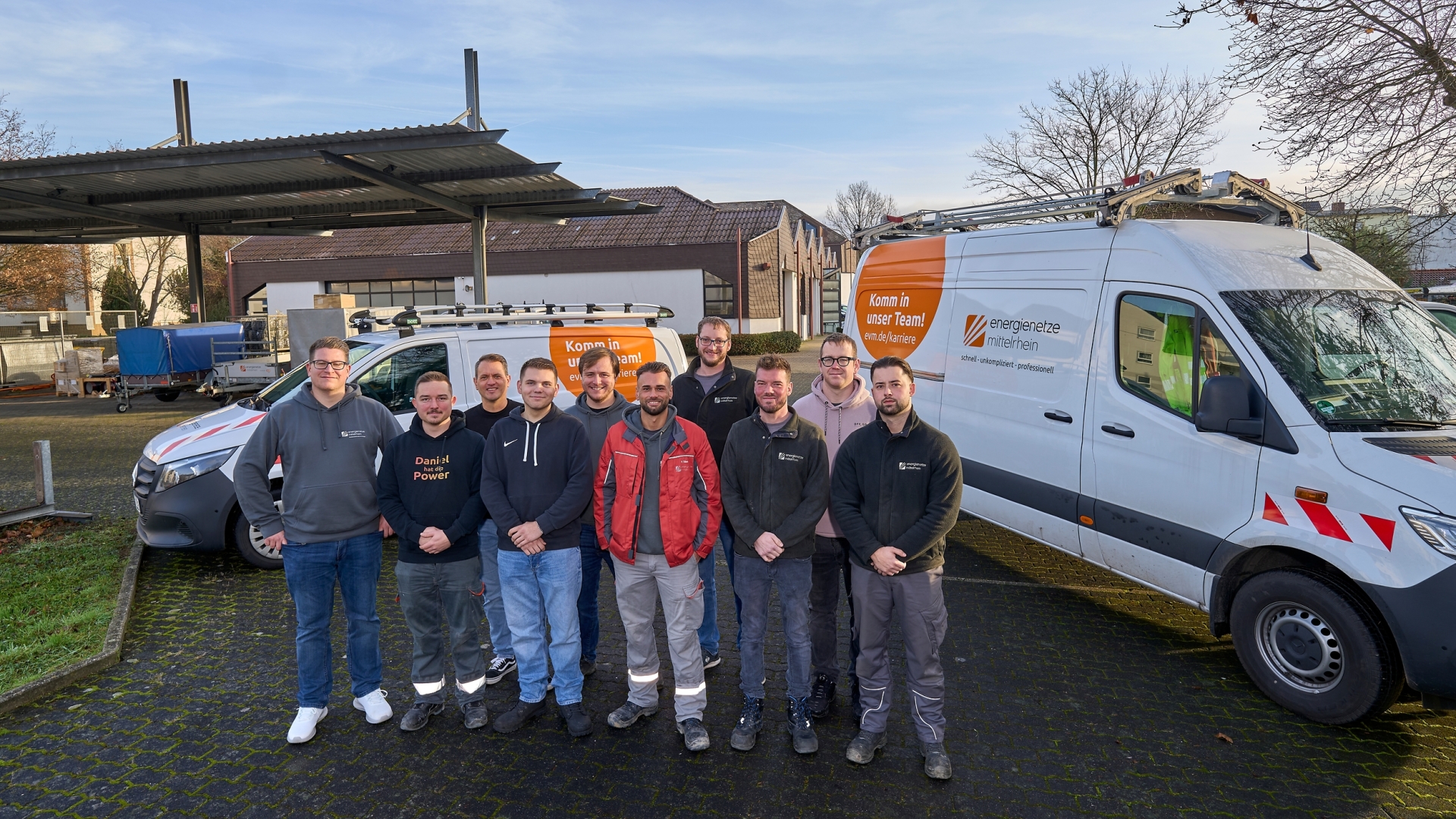 Vor zwei Dienstfahrzeugen der evm-Gruppe steht eine Gruppe Netzmonteure, die sich künftig um das Stromnetz an der Rheinschiene kümmert.