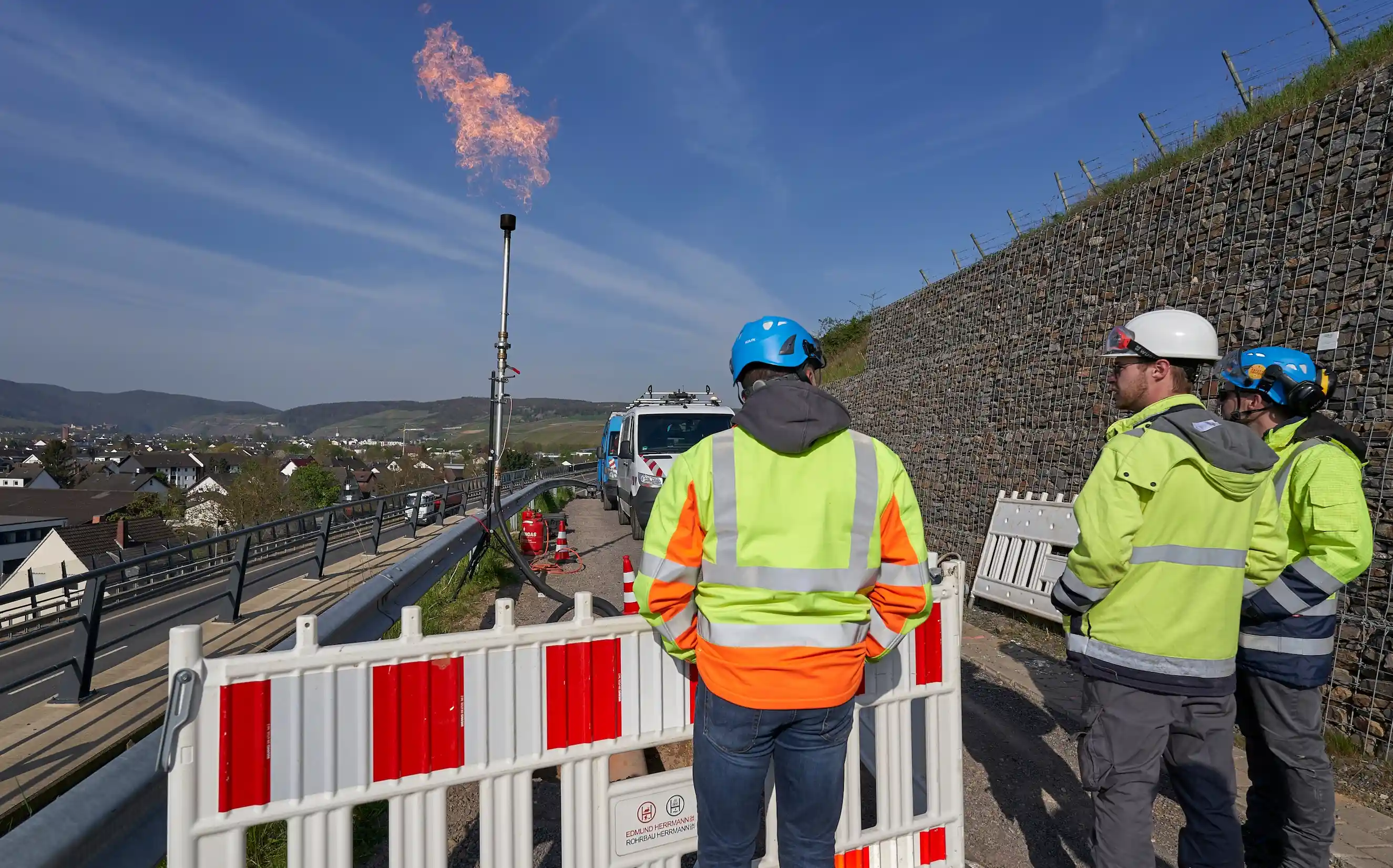Drei enm-Arbeiter in Schutzkleidung stehen vor einer Erdgasfackel.