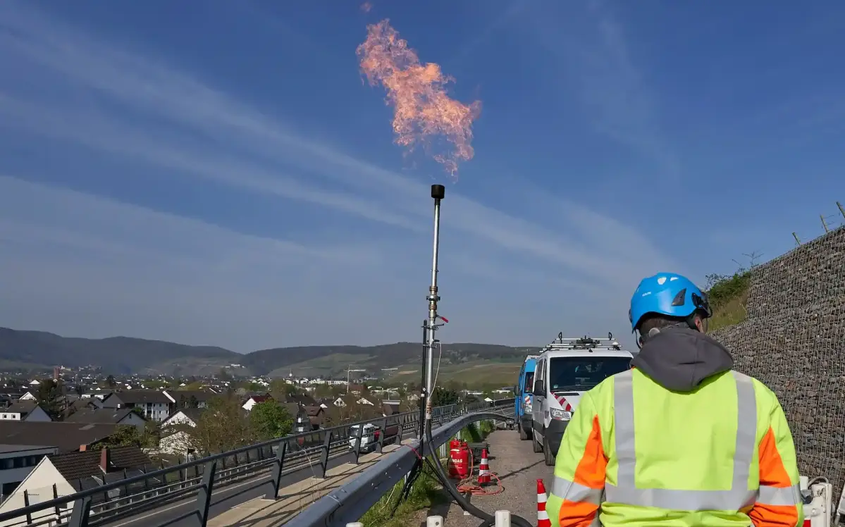 Drei enm-Arbeiter in Schutzkleidung stehen vor einer Erdgasfackel.