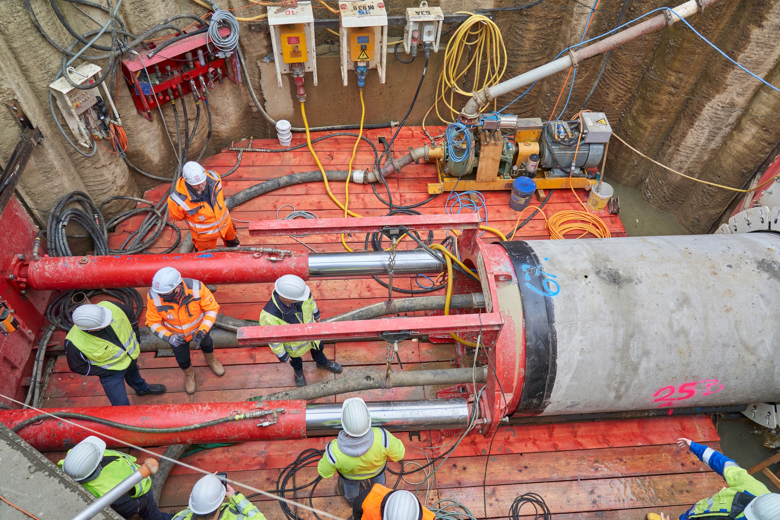Blick von oben auf einen Tunnel mit mehreren Röhren. Daneben stehen Arbeiter in Schutzkleidung
