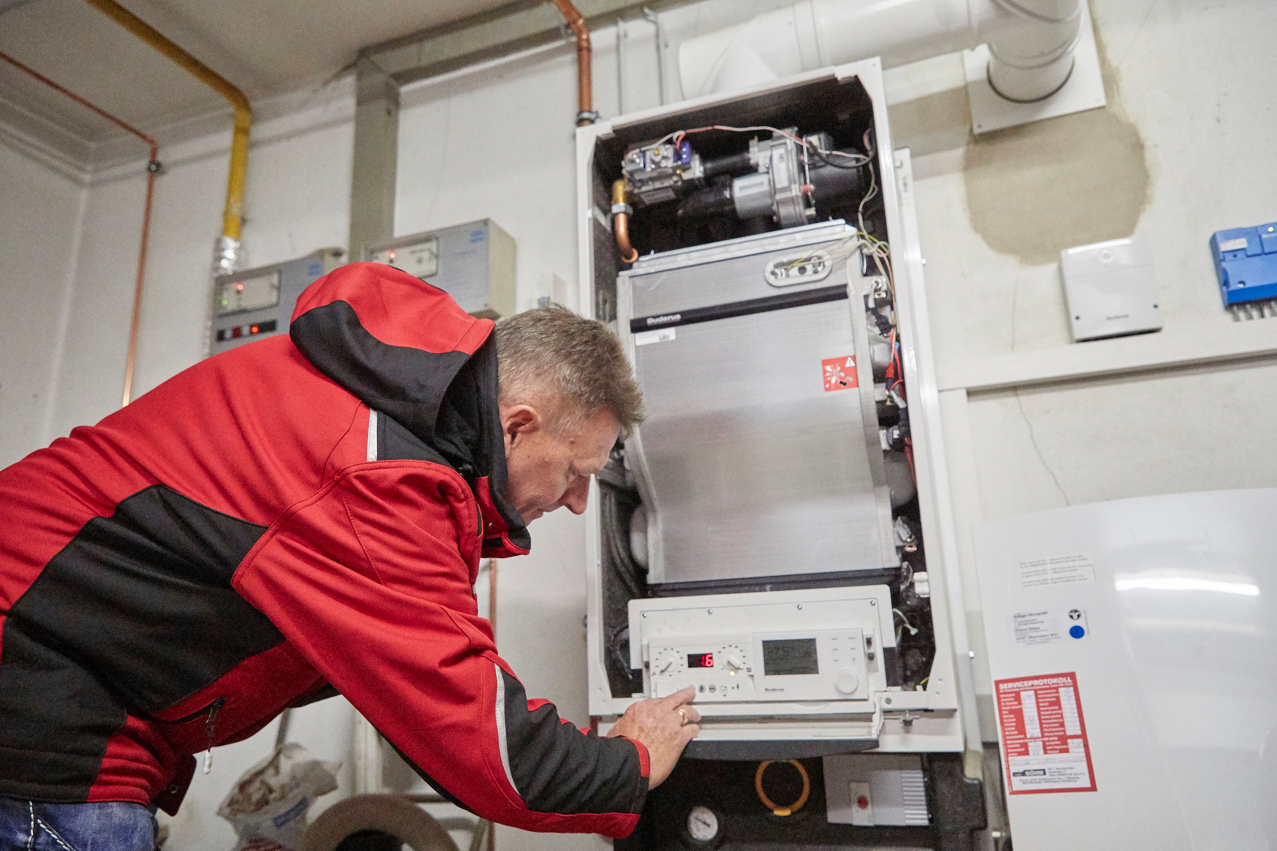 Ein Arbeiter mit einer roten Jacke arbeitet an einer Therme