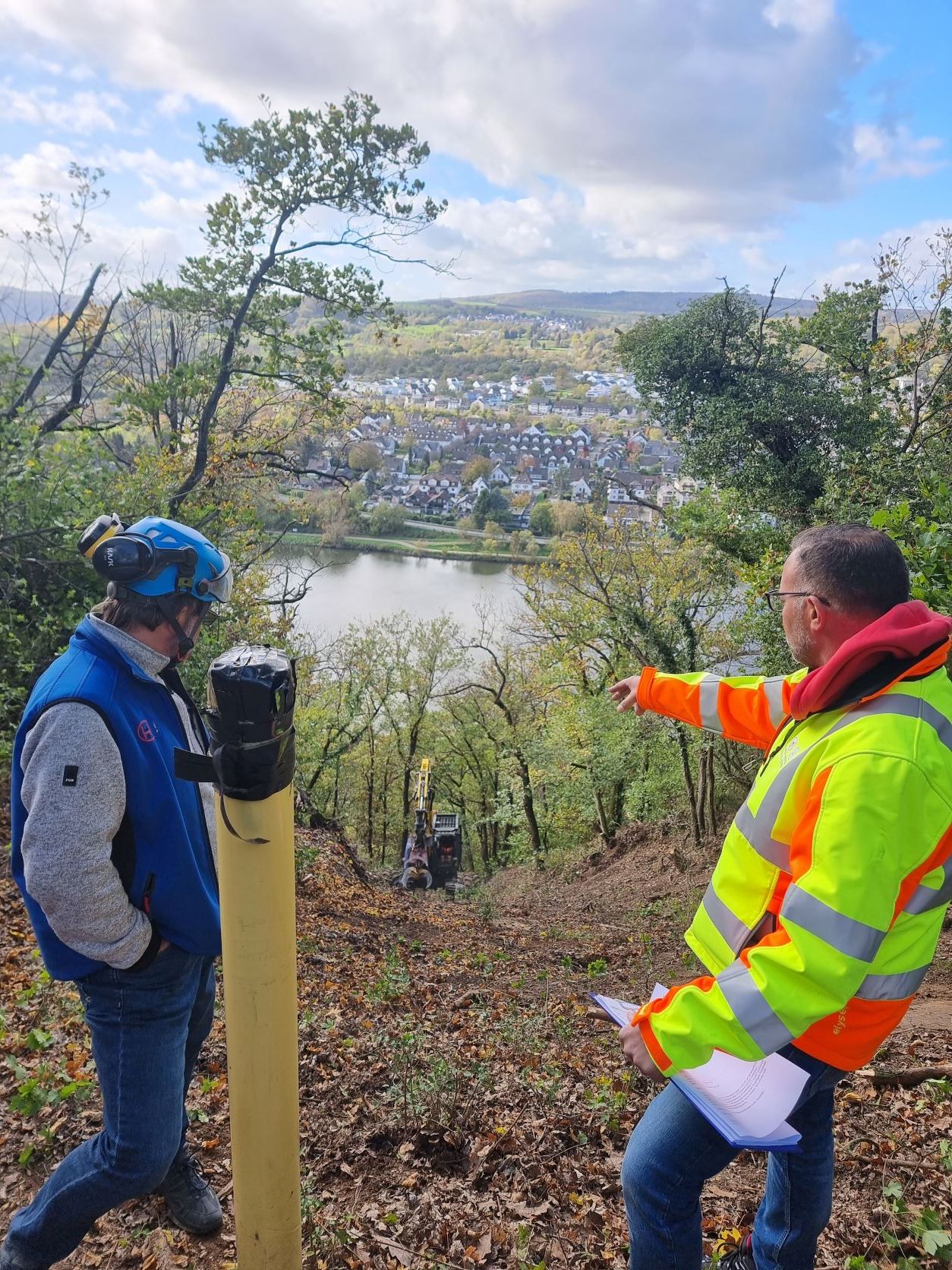 Zwei Männer mit Schutzkleidung stehen an einem Hang.