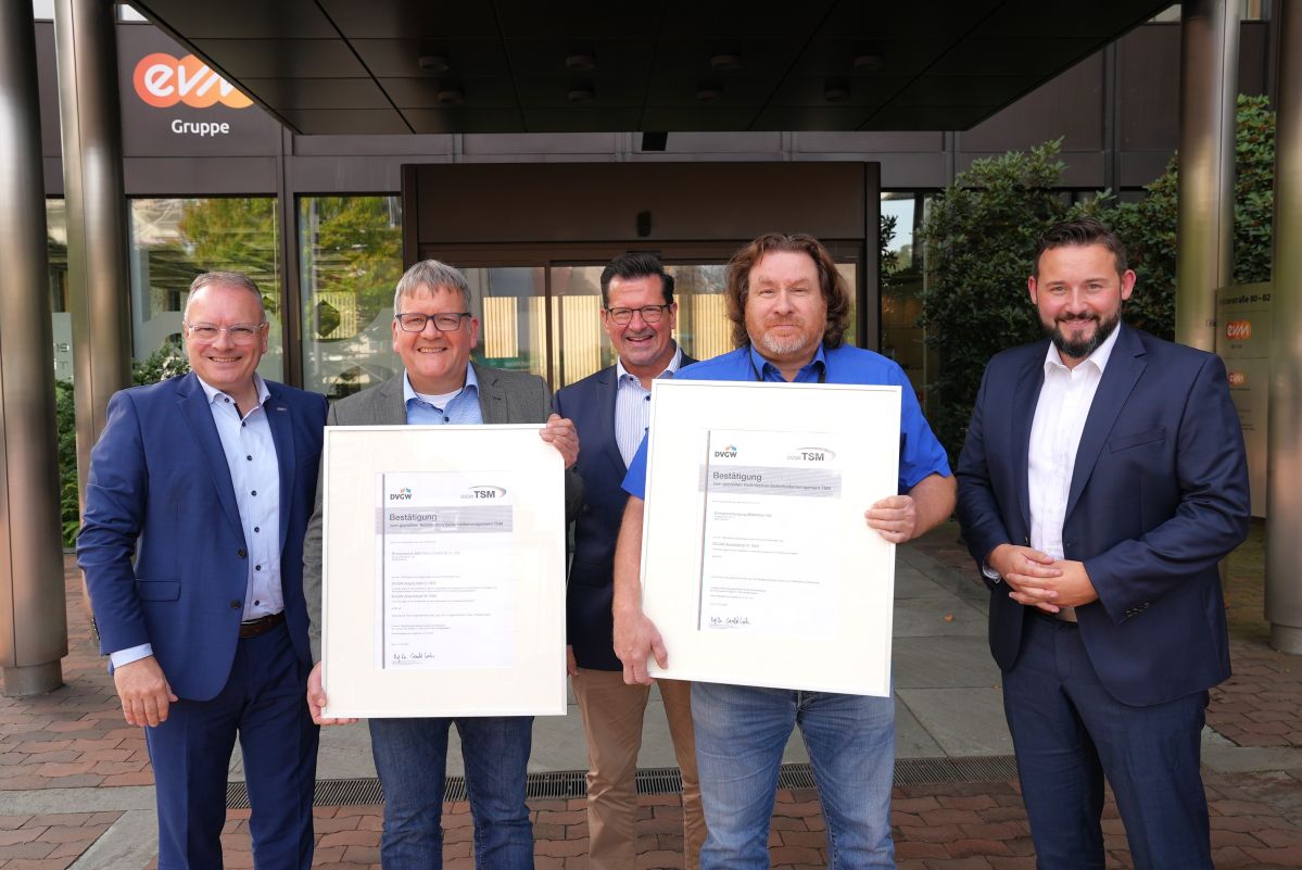 Fünf professionell gekleidete Männer lächeln freundlich und halten zwei große Bilderrahmen mit TSM-Ukrunden.