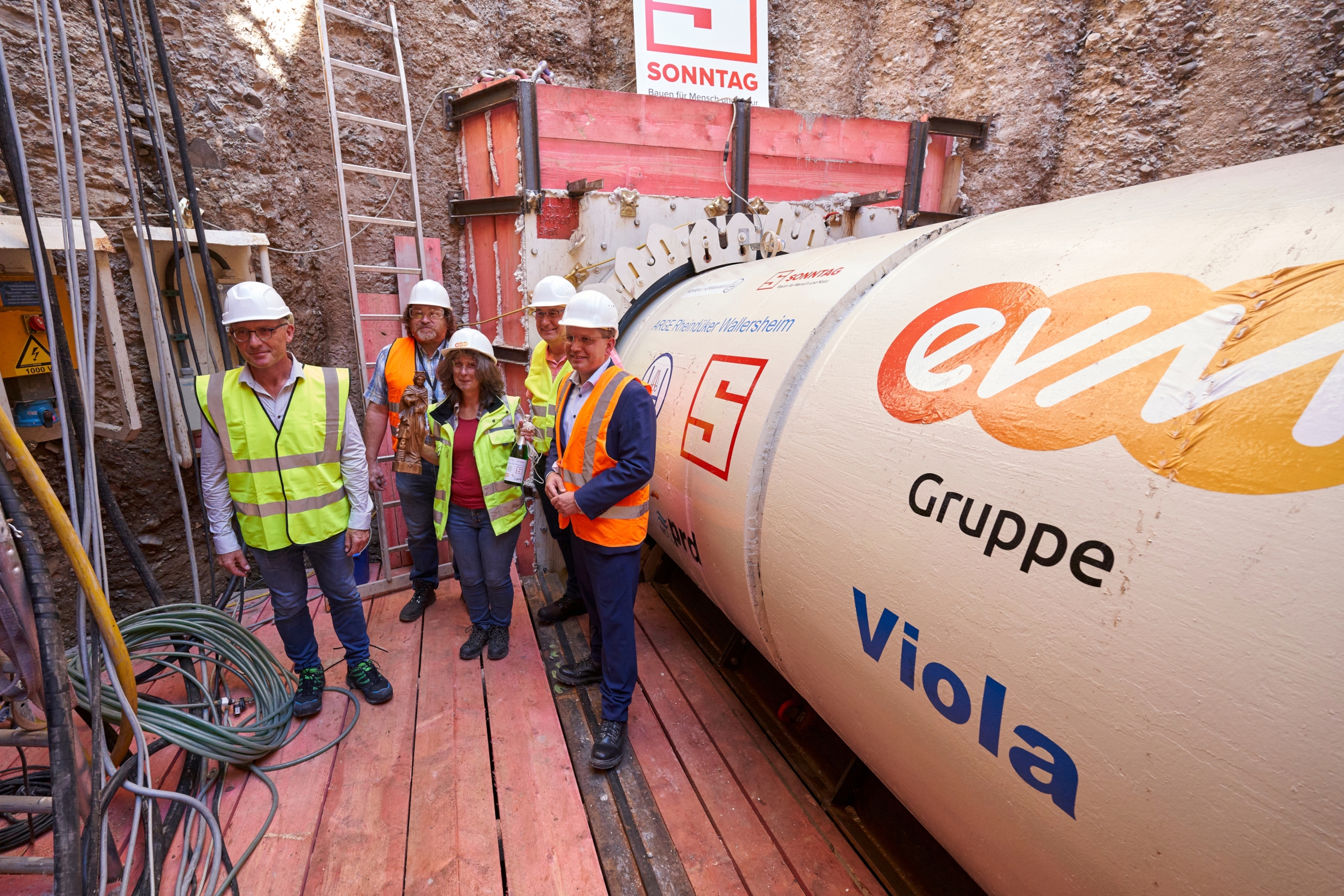 Vier Männer und eine Frau tragen Schutzwesten und Helme und lächeln freundlich.
