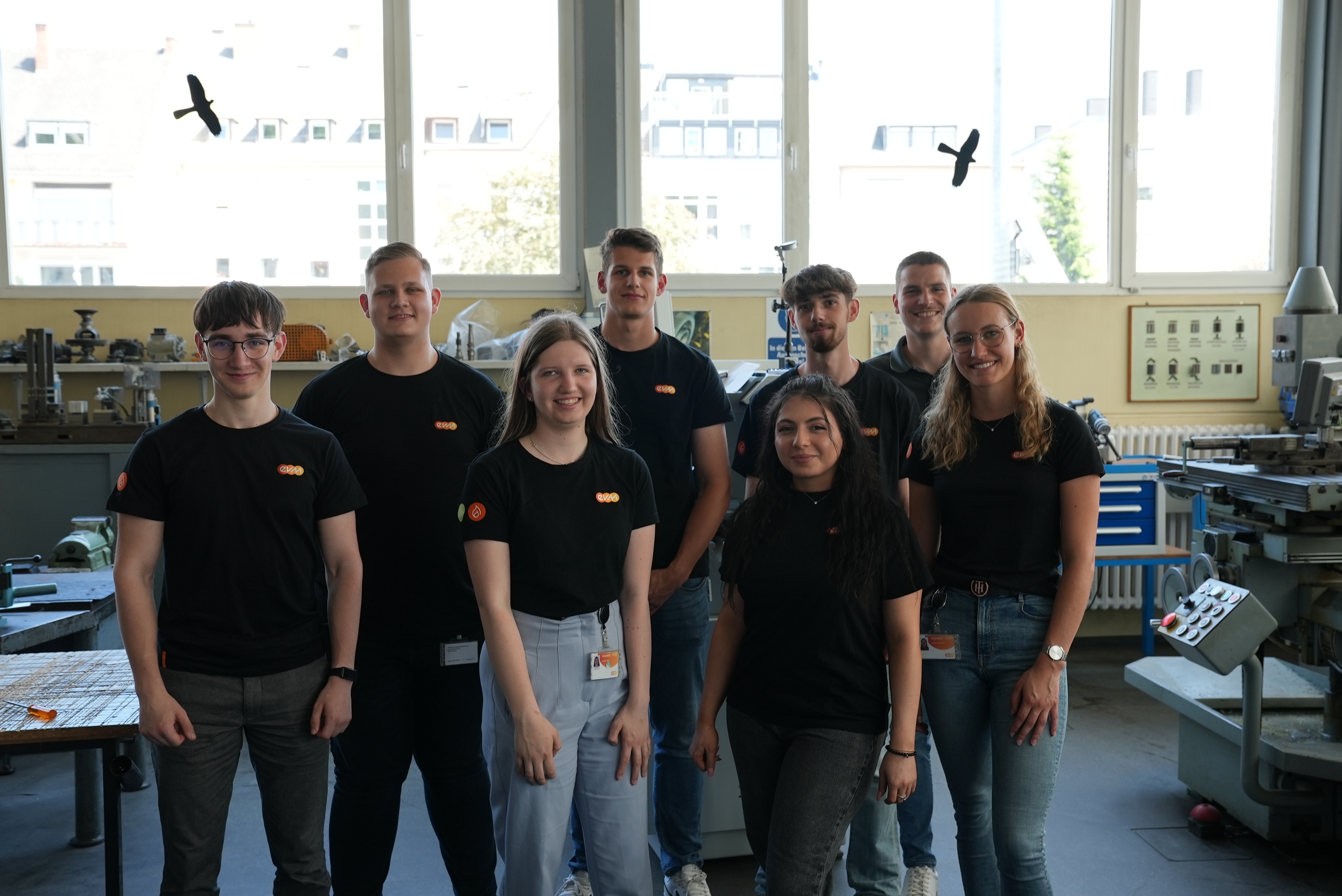 Fünf junge Männer und drei junge Frauen lächeln freundlich und tragen schwarze T-Shirts mit der Aufschrift "evm".