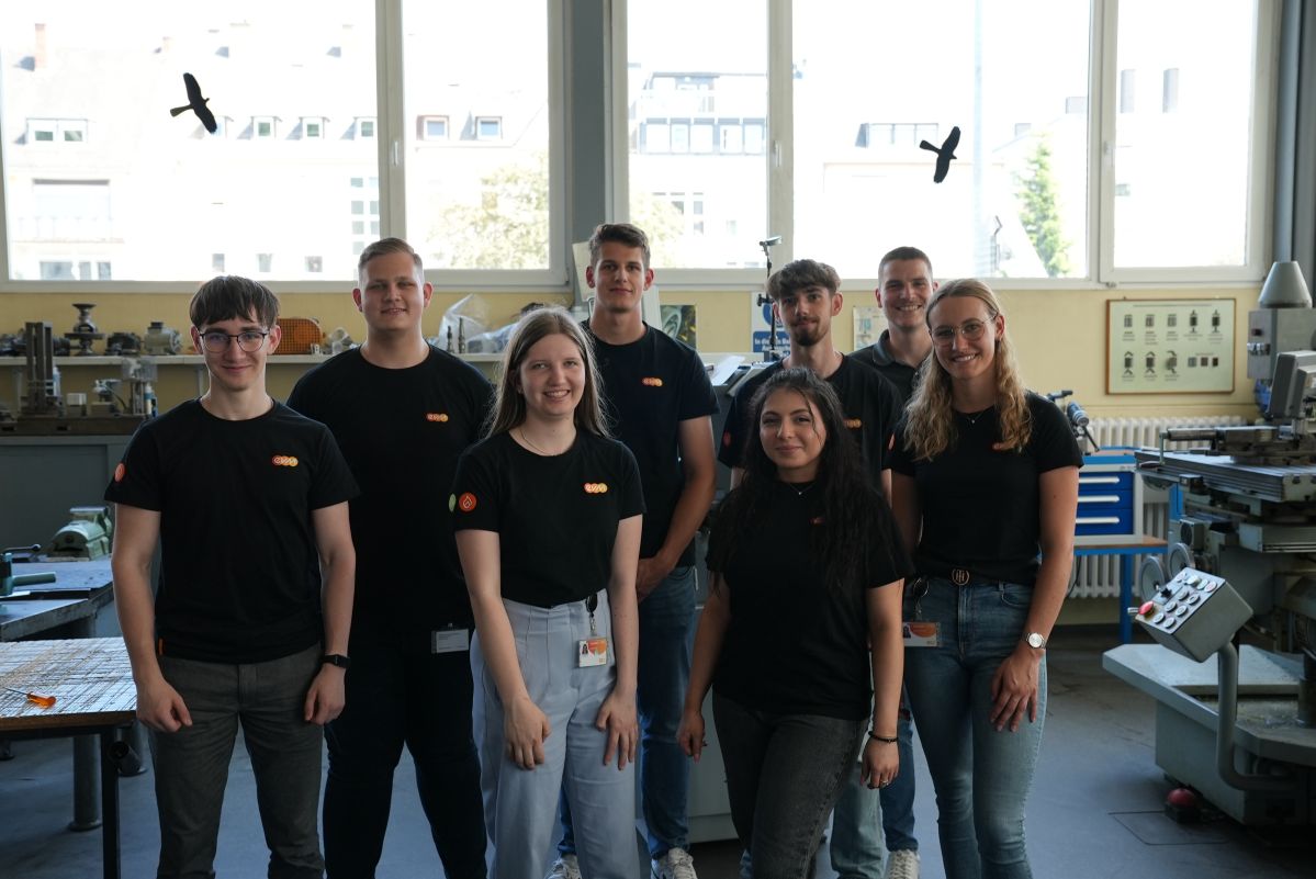 Fünf junge Männer und drei junge Frauen lächeln freundlich und tragen schwarze T-Shirts mit der Aufschrift "evm".