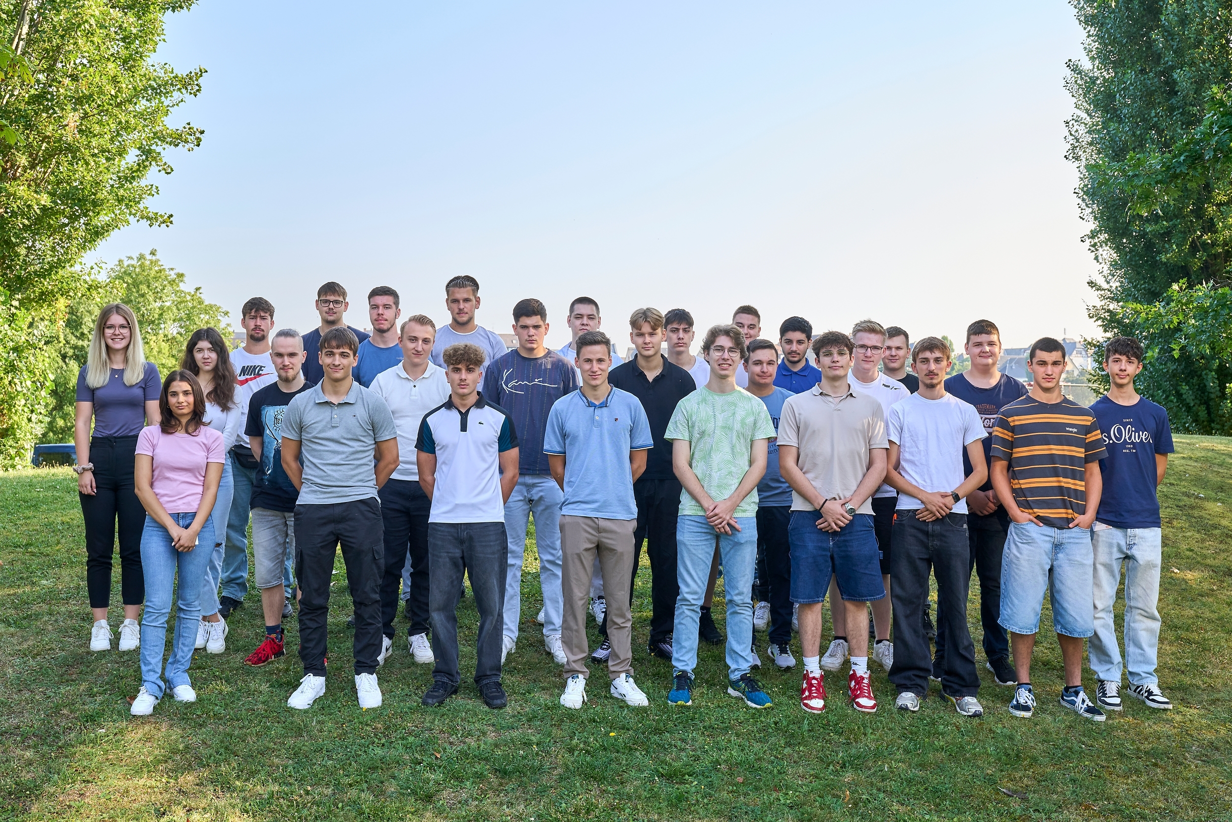 Mehrere junge Menschen stehen auf einer Wiese und lächeln freundlich