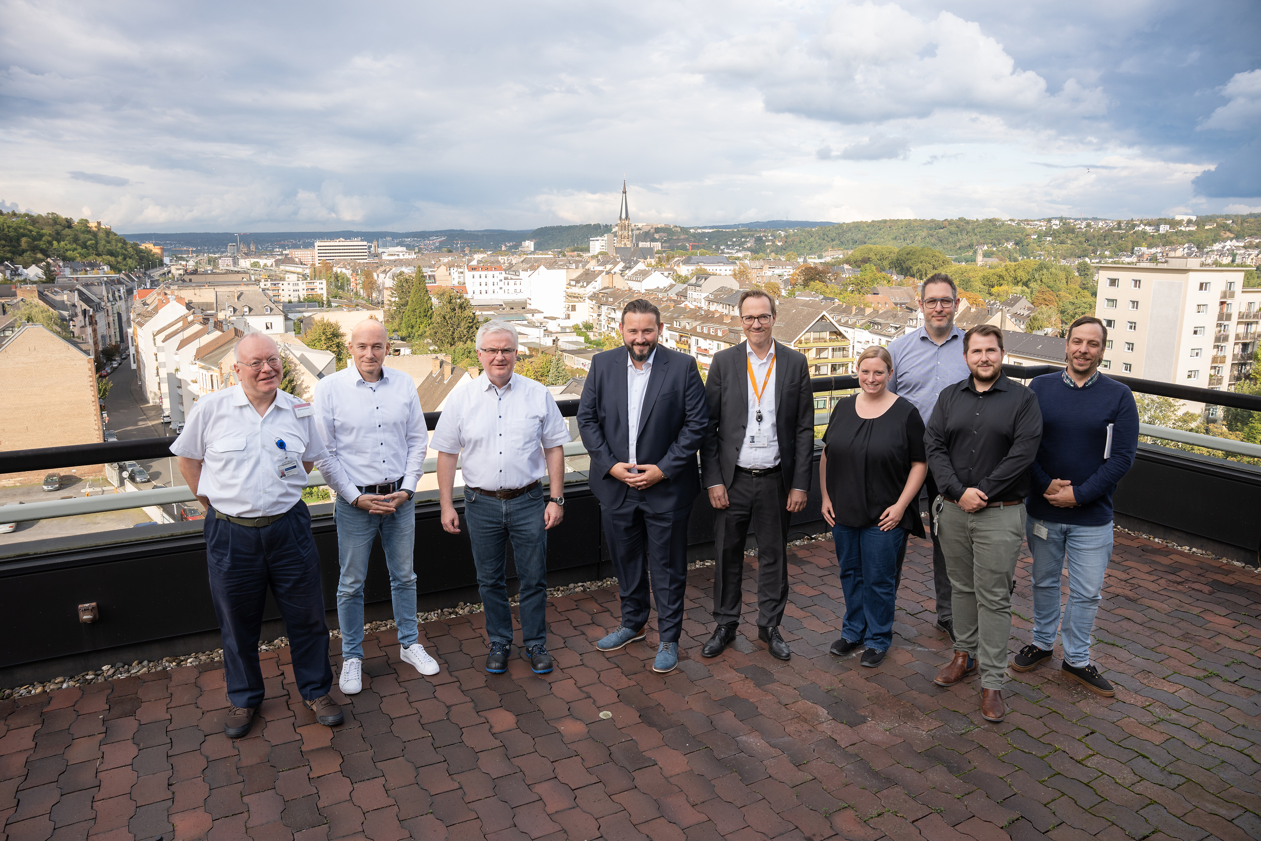 Acht Männer und eine Frau stehen auf einem Dach und lächeln freundlich
