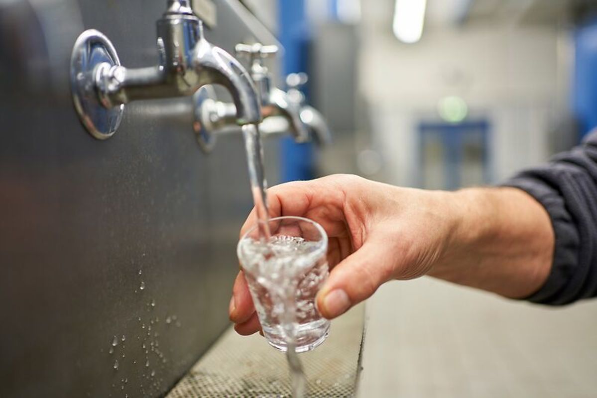 Eine Hand hält ein Wasserglas unter eine Trinkleitung