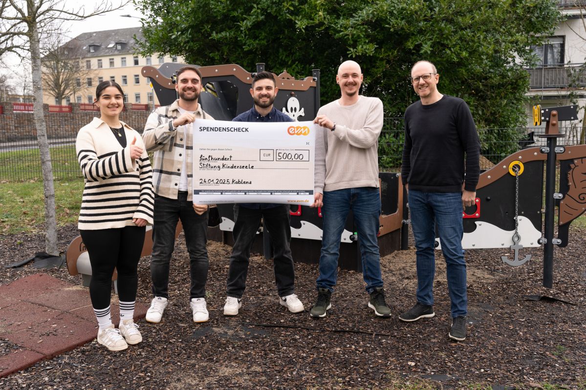 4 Männer und eine Frau stehen freundlich lächelnd vor einem Spielplatz. Sie halten ein großes Plakat auf dem "Spendencheck evm" und der Beitrag von 500 Euro stehen.