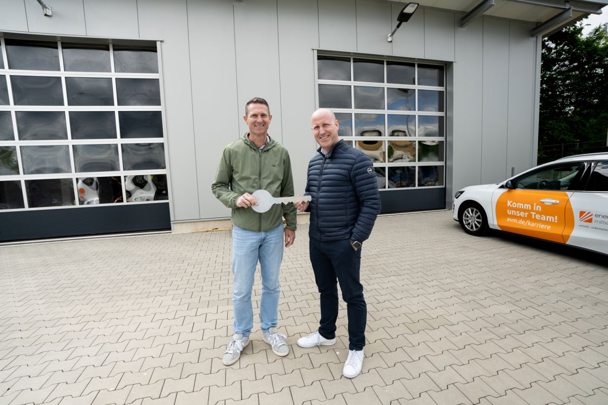 Zwei Männer stehen vor einer Lagerhalle und halten einen großen Schlüssel.