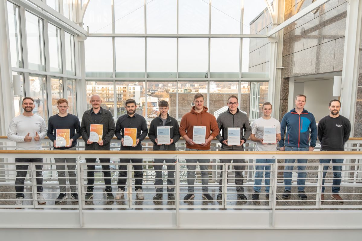 Mehrere junge Männer stehen auf einem Übergang und halten Urkunden in der Hand.