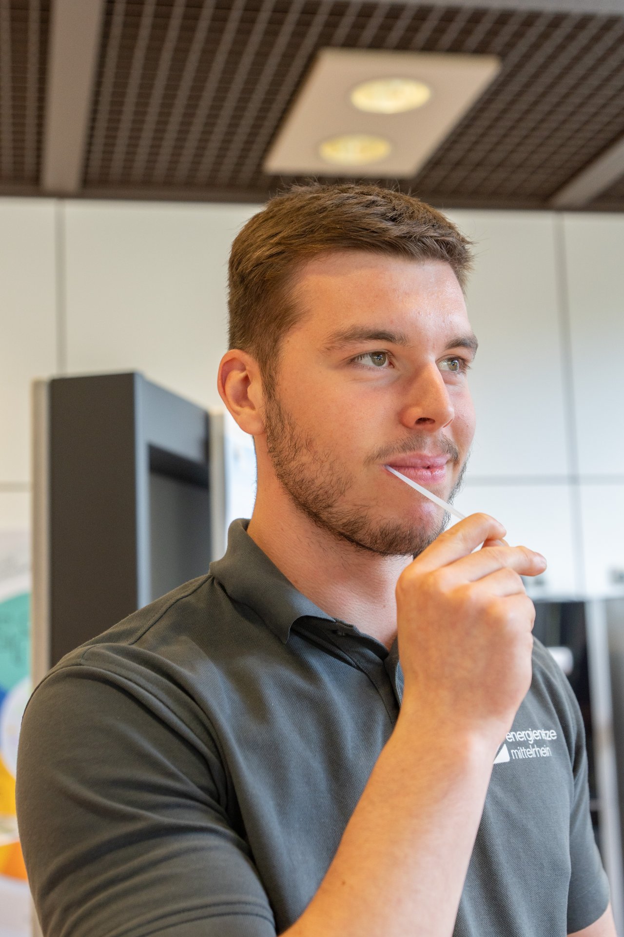 Ein Mann mit einem grauen enm Poloshirt hat ein schmales weißes Stäbchen im Mund.