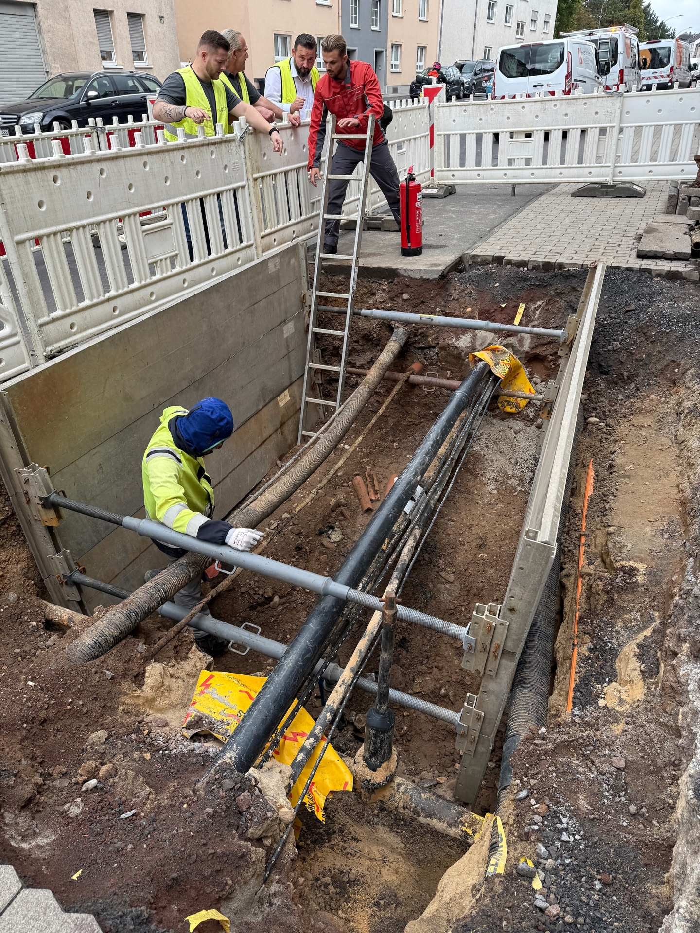 Mehrere Arbeiter in Schutzkleidung befinden sich auf einer Baustelle mit freigelegten Rohren.