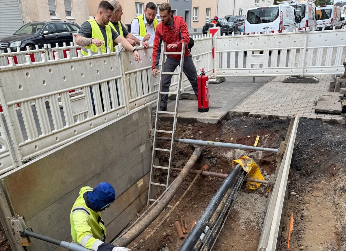 Mehrere Arbeiter in Schutzkleidung befinden sich auf einer Baustelle mit freigelegten Rohren.