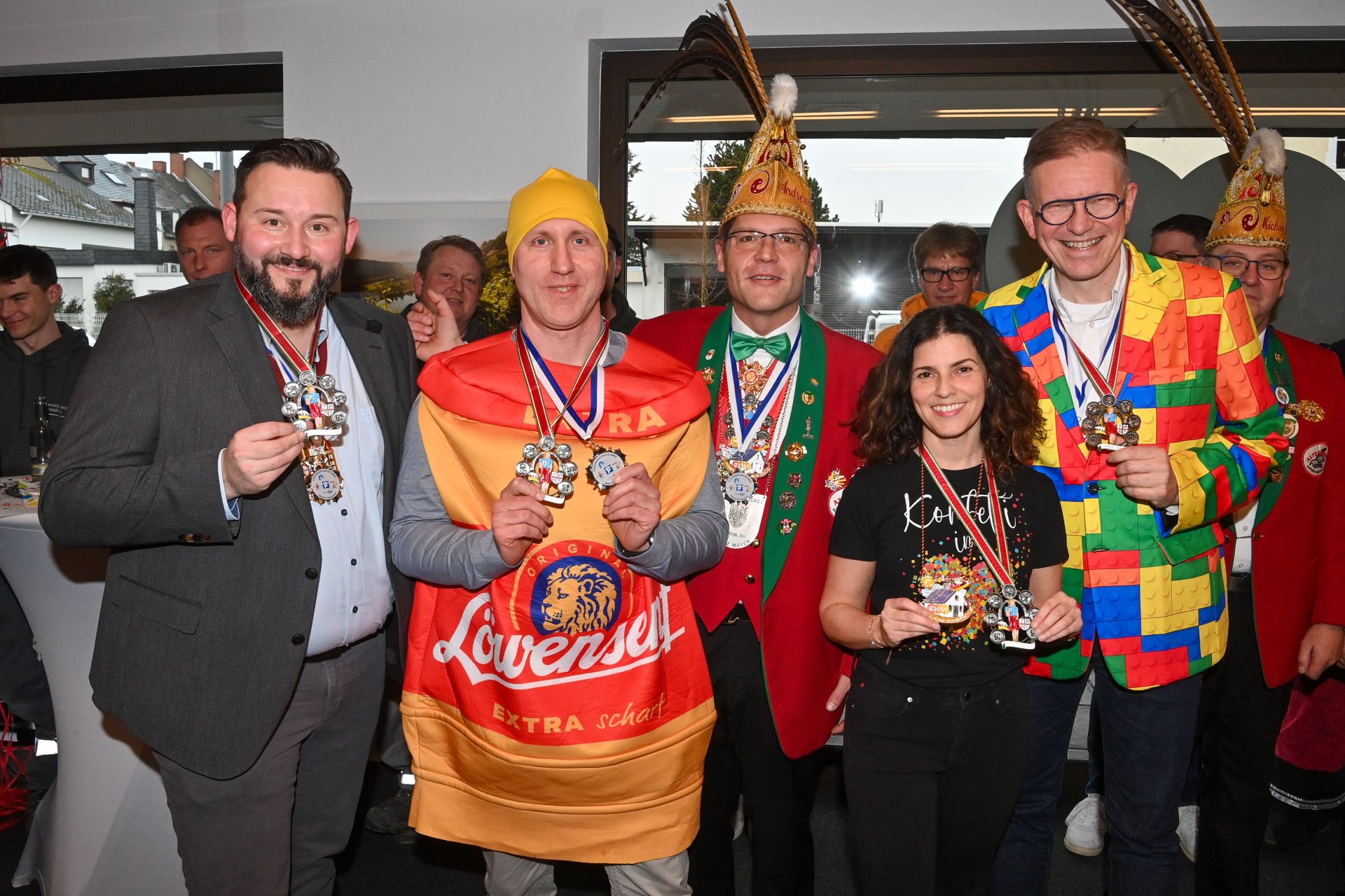 Gruppe von Vertreterinnen und Vertretern der Stadtwerke Mayen, der evm‑Gruppe und der Alten Grossen Mayener Karnevalsgesellschaft beim Karnevalsempfang im Kundenzentrum, in farbenfrohen Kostümen und mit verliehenen Karnevalsorden.