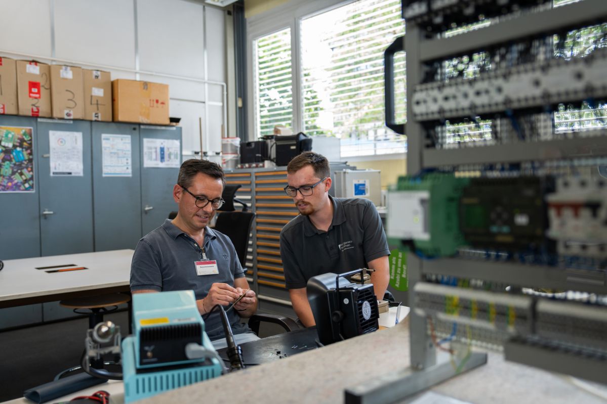 David Langner sitzt gemeinsam mit einem Mitarbeiter der Energienetze Mittelrhein in der Ausbildungswerkstatt an einem Arbeitstisch. Vor ihnen befinden sich elektronische Bauteile und eine Übungsanlage für die Elektrotechnik. Während seines Praktikumstags erhielt der Oberbürgermeister Einblicke in die Ausbildung und technische Arbeitsbereiche der evm-Gruppe.